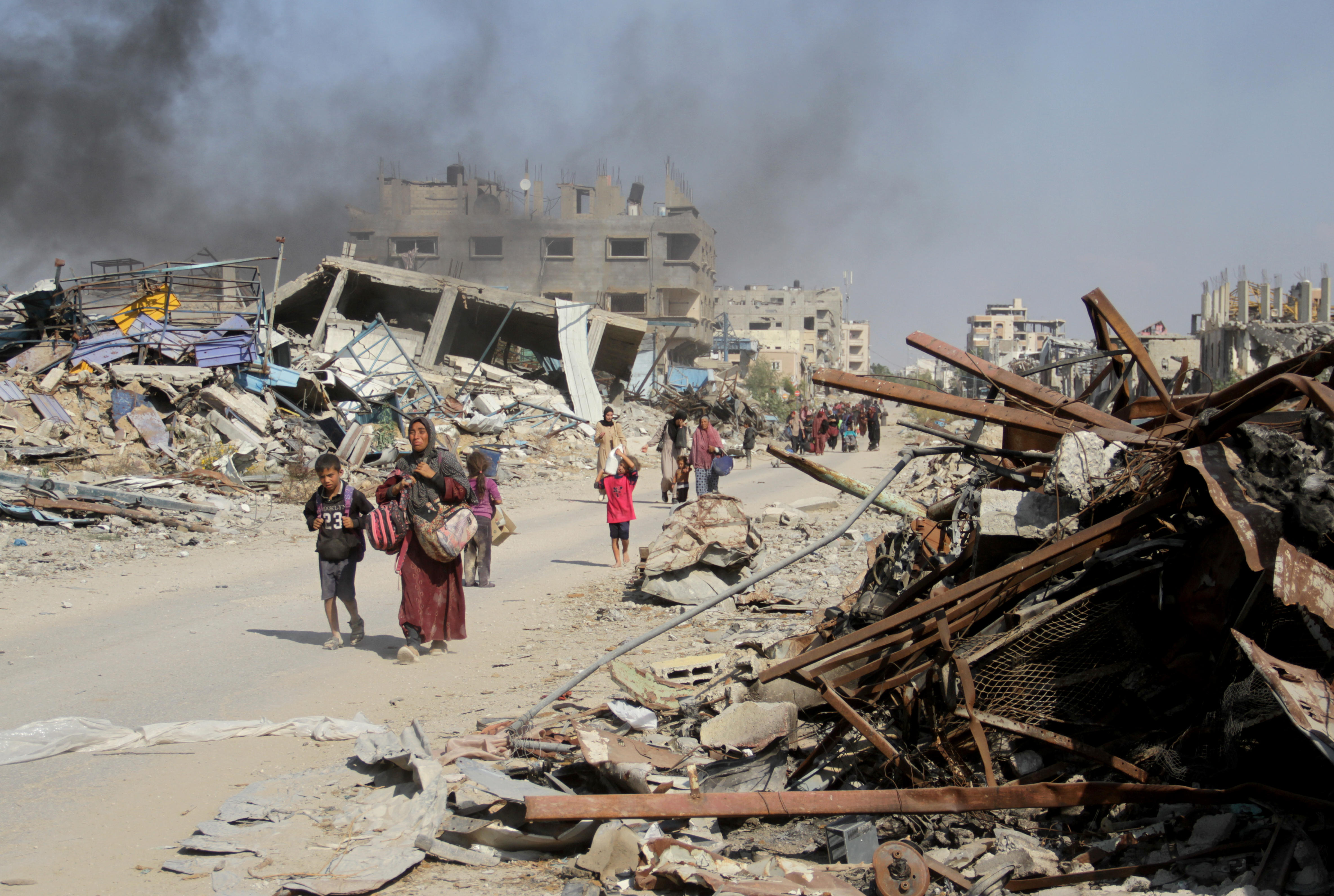 Evacuation from north Gaza. (Photo: picture alliance / Anadolu | M. İssa) Families walk along a road through destroyed buildings and rubble. There is black smoke in the air.
