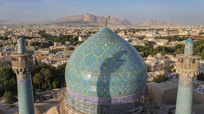 Sheikh Lotfollah Mosque in Isfahan, Iran. (Photo: Picture Alliance / Amazing Aerial Agency | Airpano) A mosque dome with green mosaic tiles against the backdrop of a city, with mountains in the background.