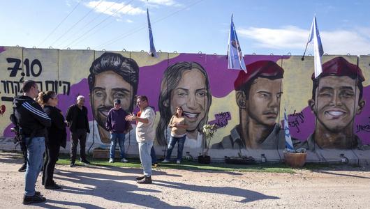 Gaza is separated from Israeli territory in places by concrete walls. Photo: Picture Alliance/Newscom | J. Hollander A group stands in front of a concrete wall. Colourful portraits of Israeli hostages can be seen on the wall.