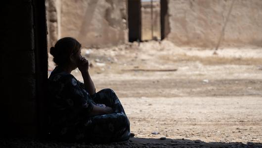 Sinjar, Iraq, August 2024. (Photo: picture alliance / Anadolu | Stringer) A silhouetted woman sits in the doorway of a ruined building looking out onto the street.